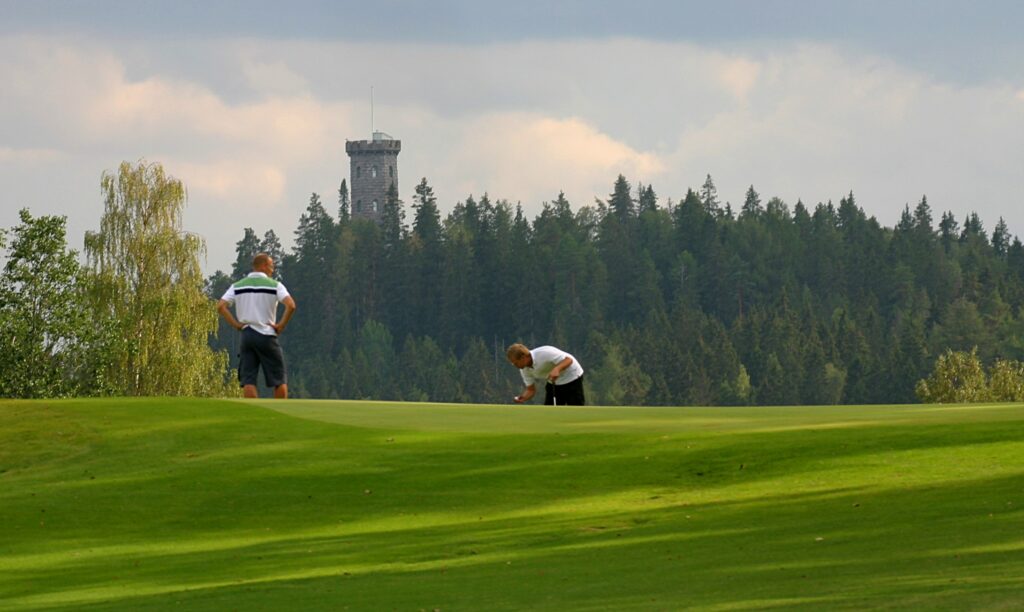 Kaksi golffaria golfkentällä, taustalla näkyy Aulangon näkötorni.