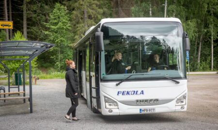 Henkilö nousemassa linja-autoon kesäisenä päivänä.