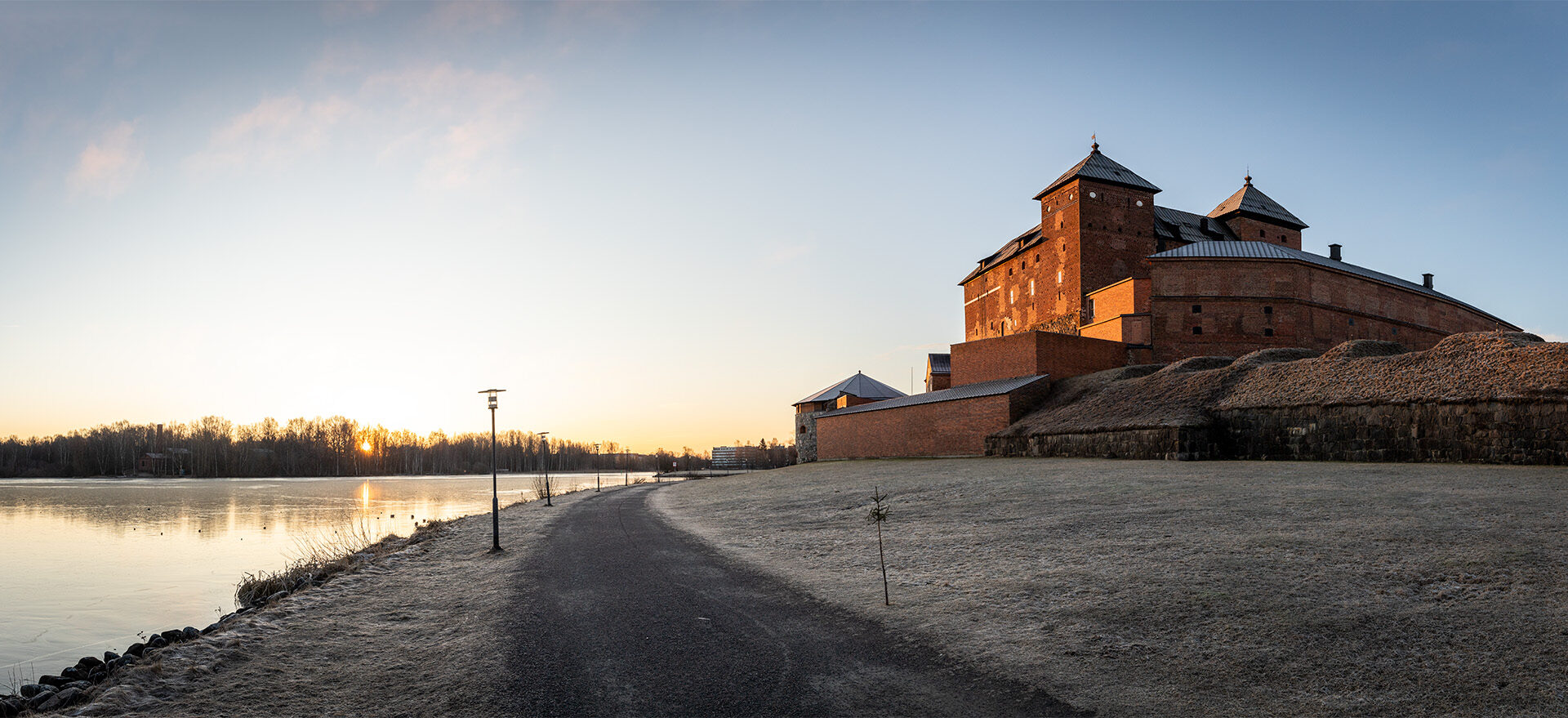 Järven rannalla sijaitseva Hämeen punatiilinen linna, jonka edessä oleva nurmialue on kuuran peitossa.