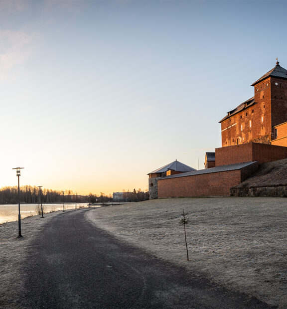 Järven rannalla sijaitseva Hämeen punatiilinen linna, jonka edessä oleva nurmialue on kuuran peitossa.